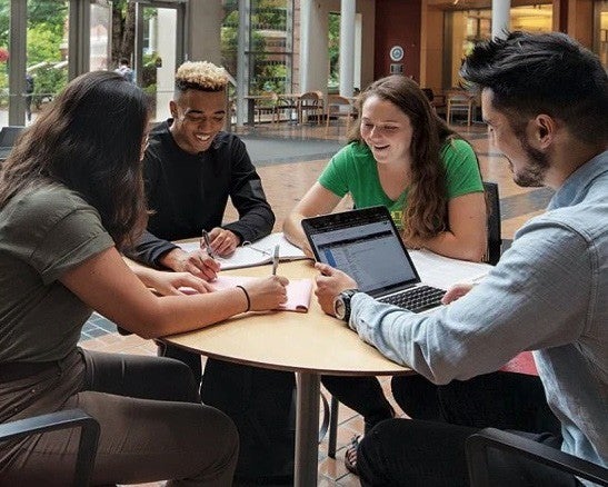 Four students studying with a laptop and paper around a table in Lillis Hall.