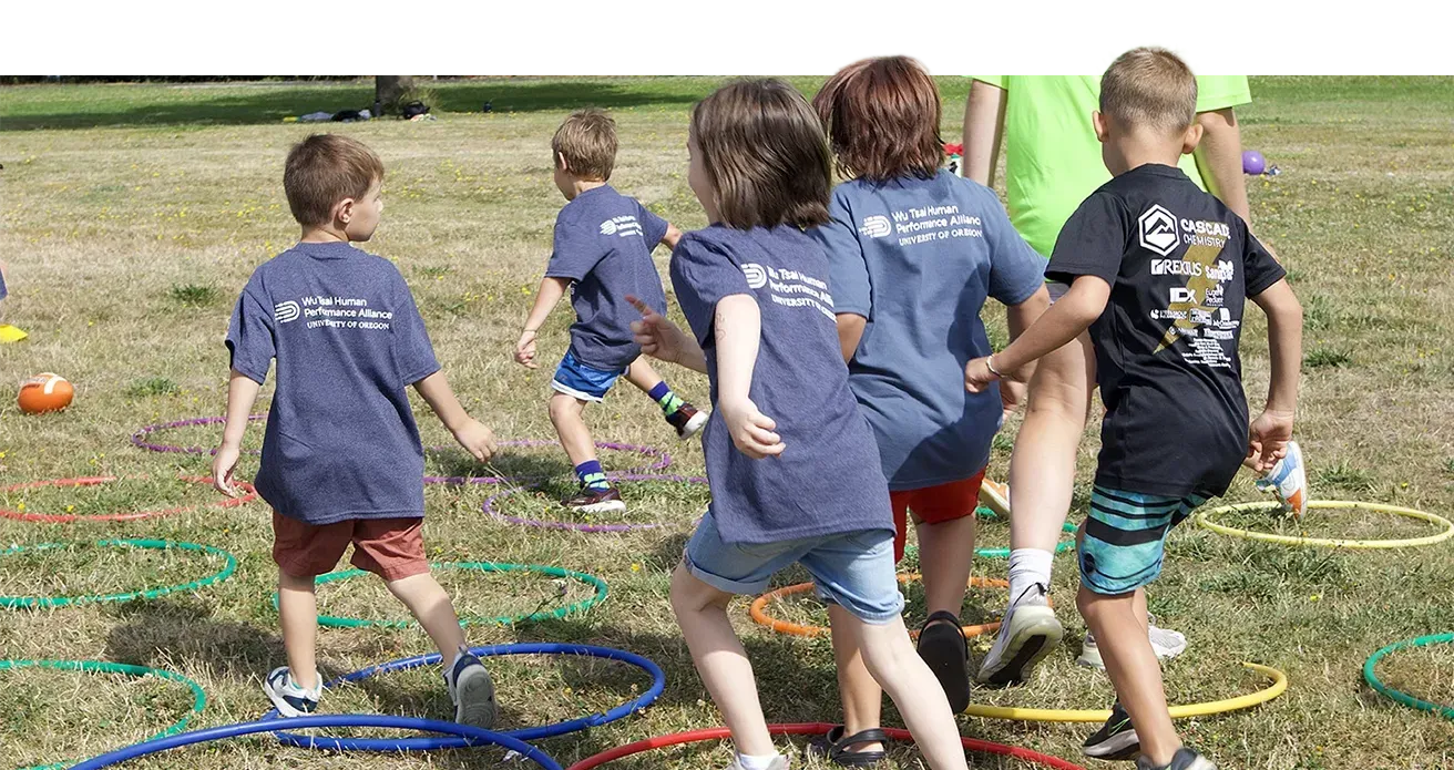 children running over hula hoops in a grassy area during a camp
